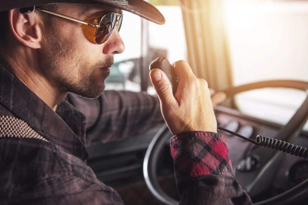 A truck driver using a high-tech two-way radio while driving, showcasing in-cab communication equipment in a New Zealand freight vehicle.